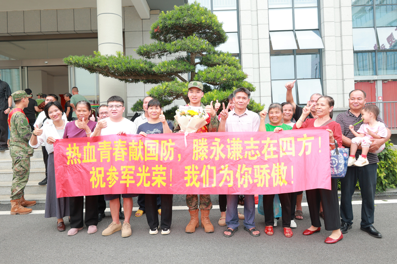 新兵滕永谦的家人亲友齐聚现场，拉起横幅，为即将奔赴军营的他送上祝福。学校供图